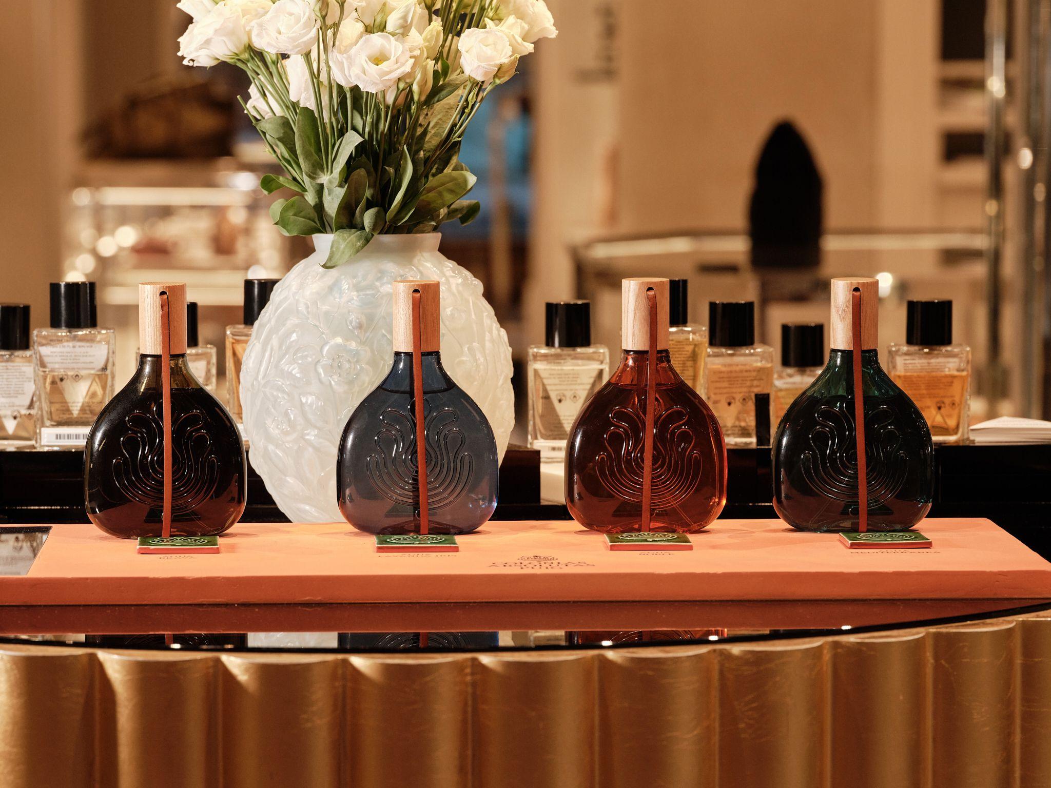 Four Colonias Absolutas Puig fragrance bottles displayed on a counter beside a vase of white roses
